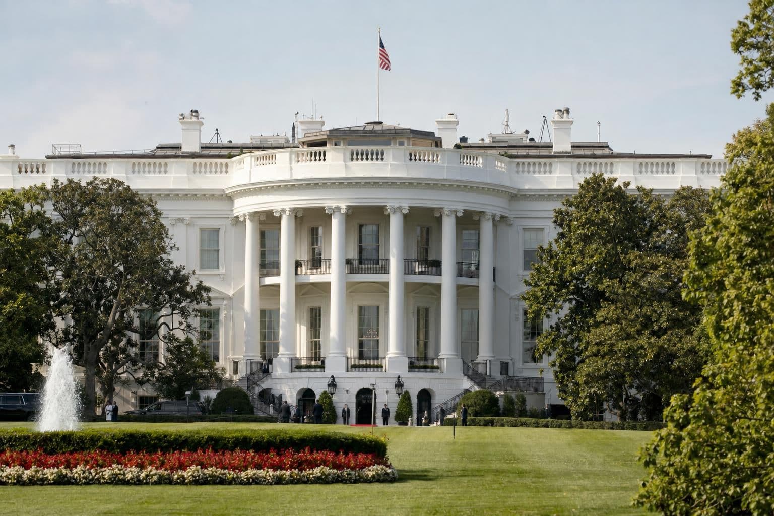 The White House in Washington seen from across its lawn, with small, distant figures near the entrance.