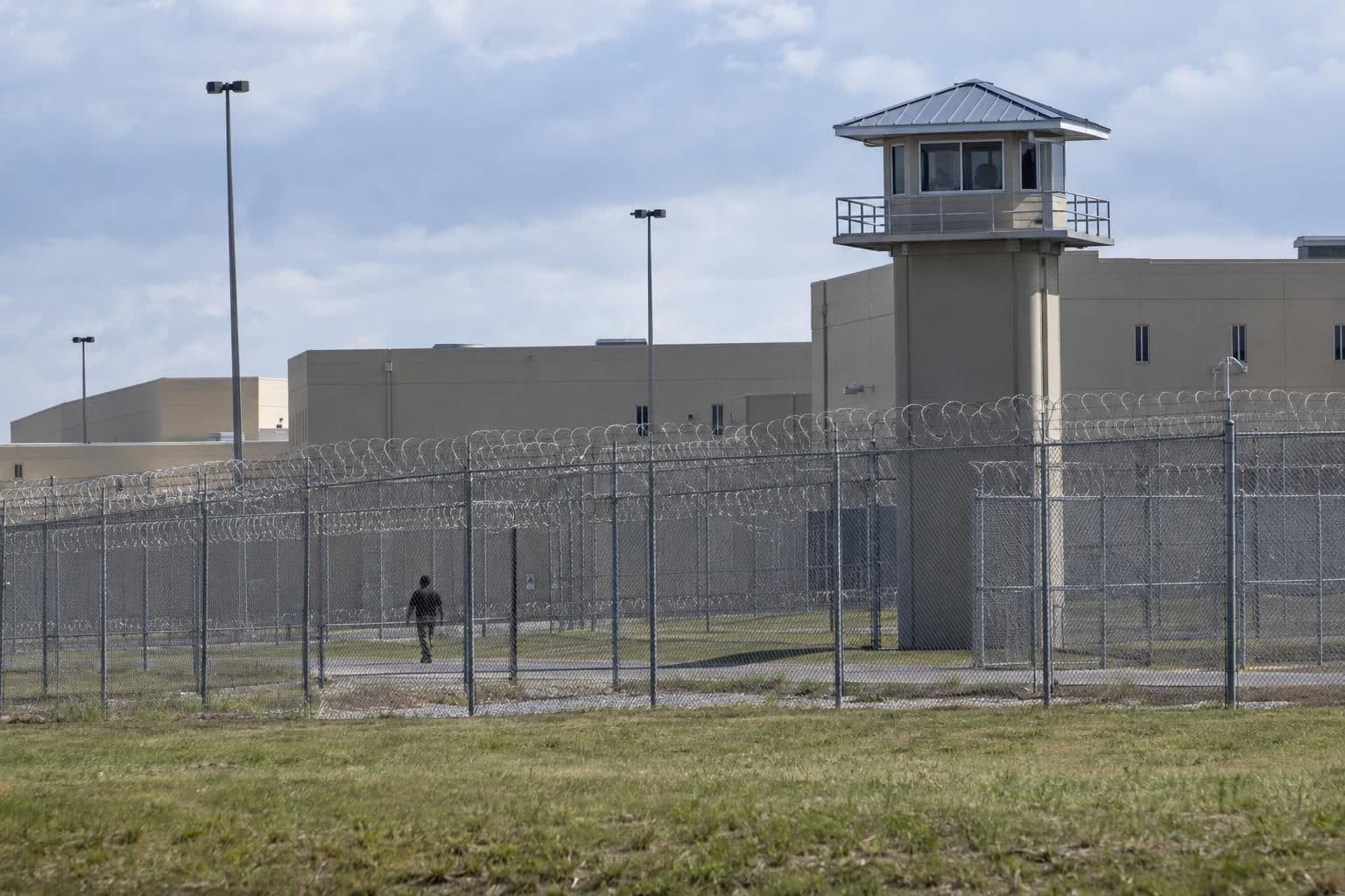 An institutional prison building stands behind a secure perimeter fence.