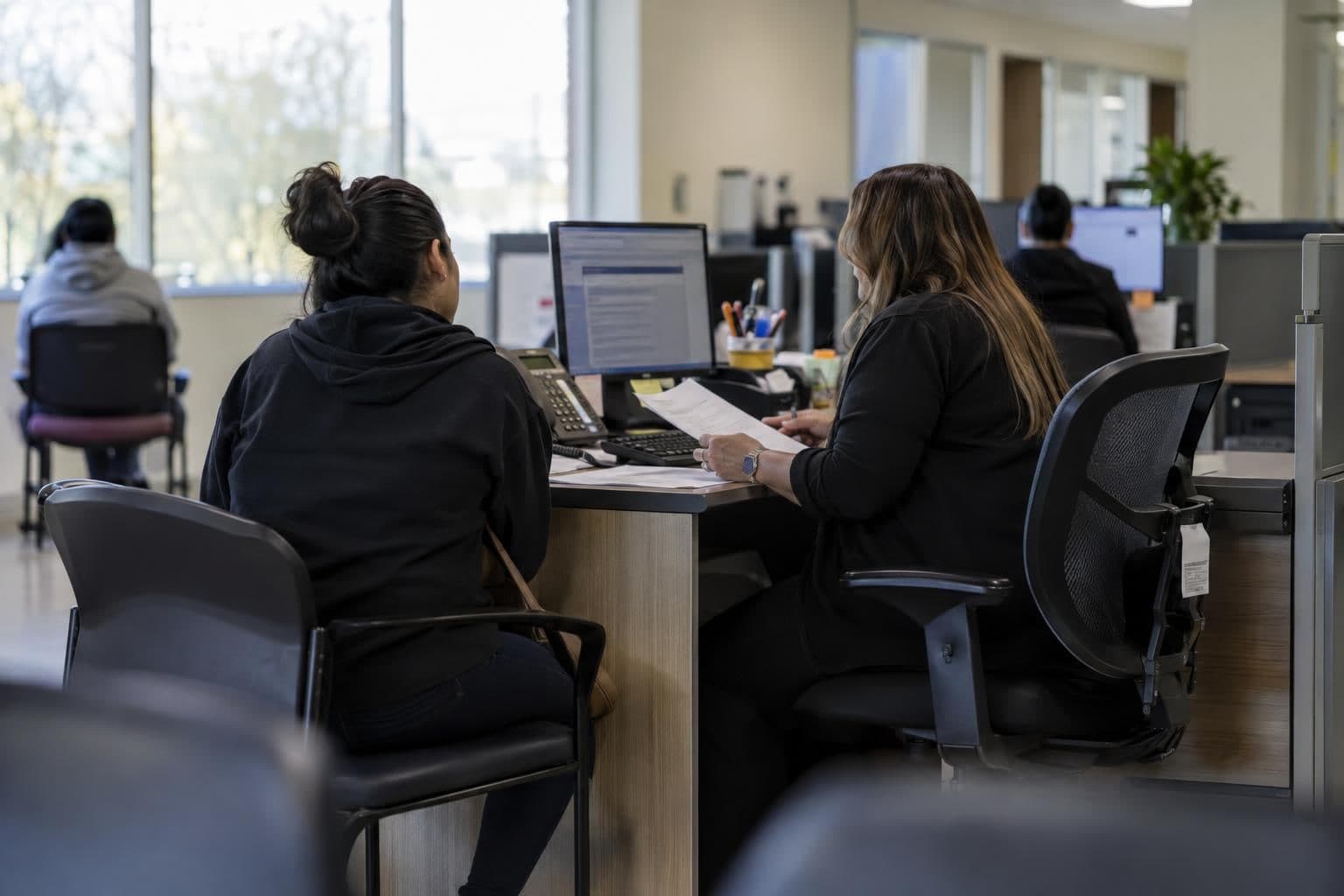 An enrollment worker reviews health coverage paperwork with an applicant at a desk.