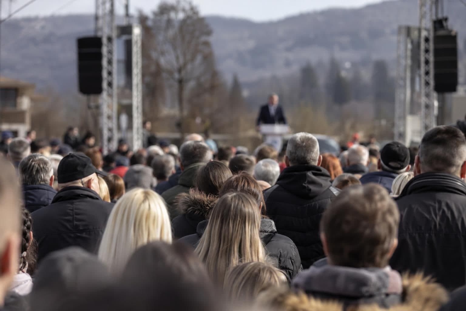 Anonymous attendees face a distant speaker at a campaign rally in Bosnia.
