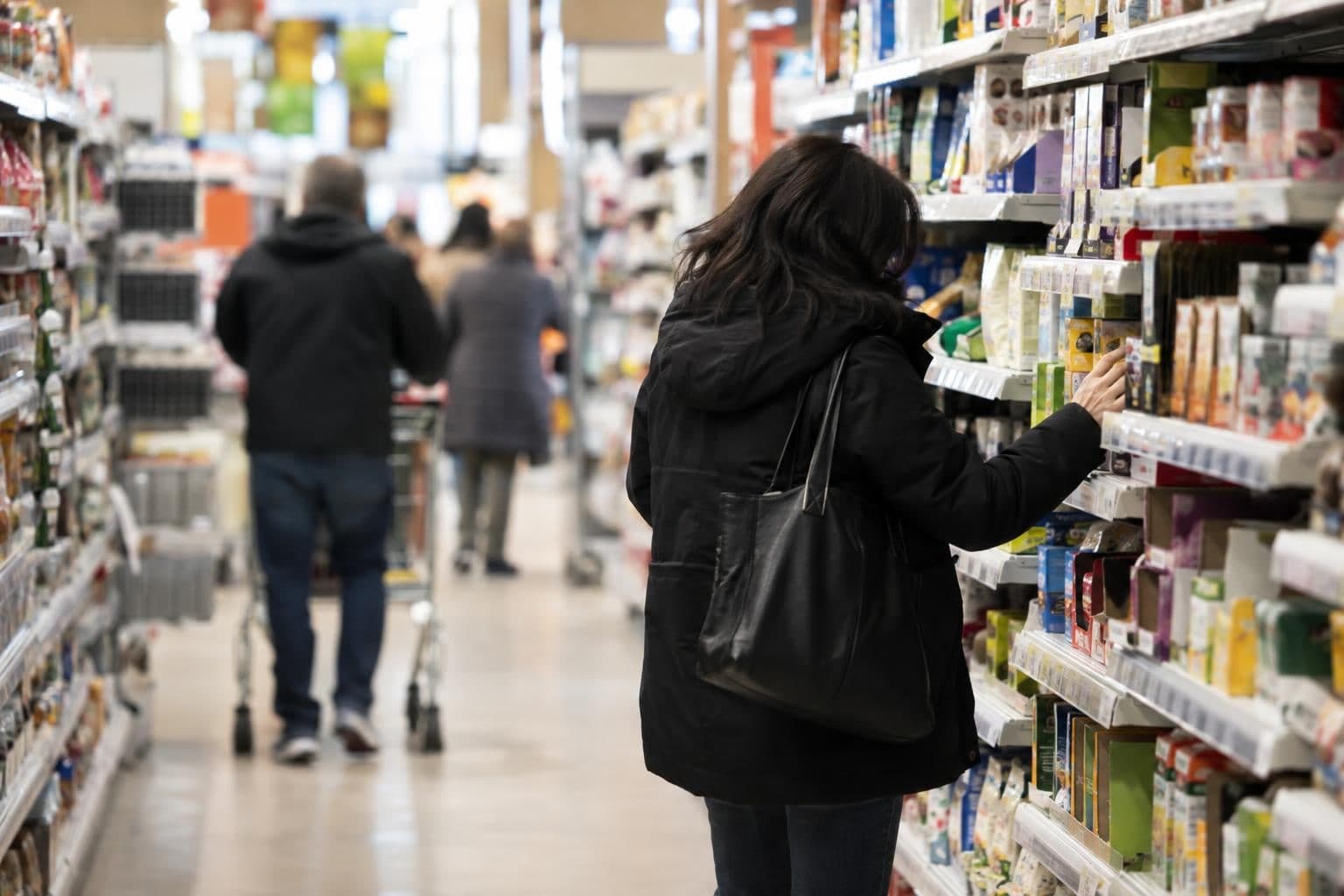 A shopper browses goods on a store shelf, illustrating consumer costs amid a tariff debate.