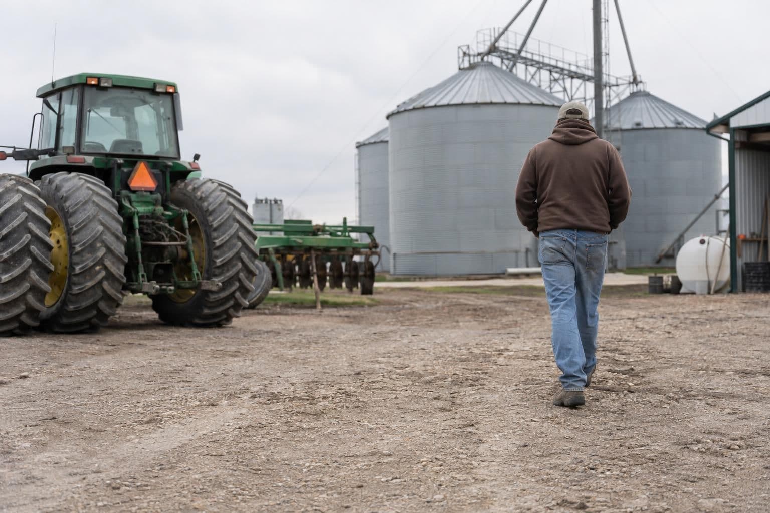 An anonymous farmer stands in an agricultural setting with farming equipment in the background.