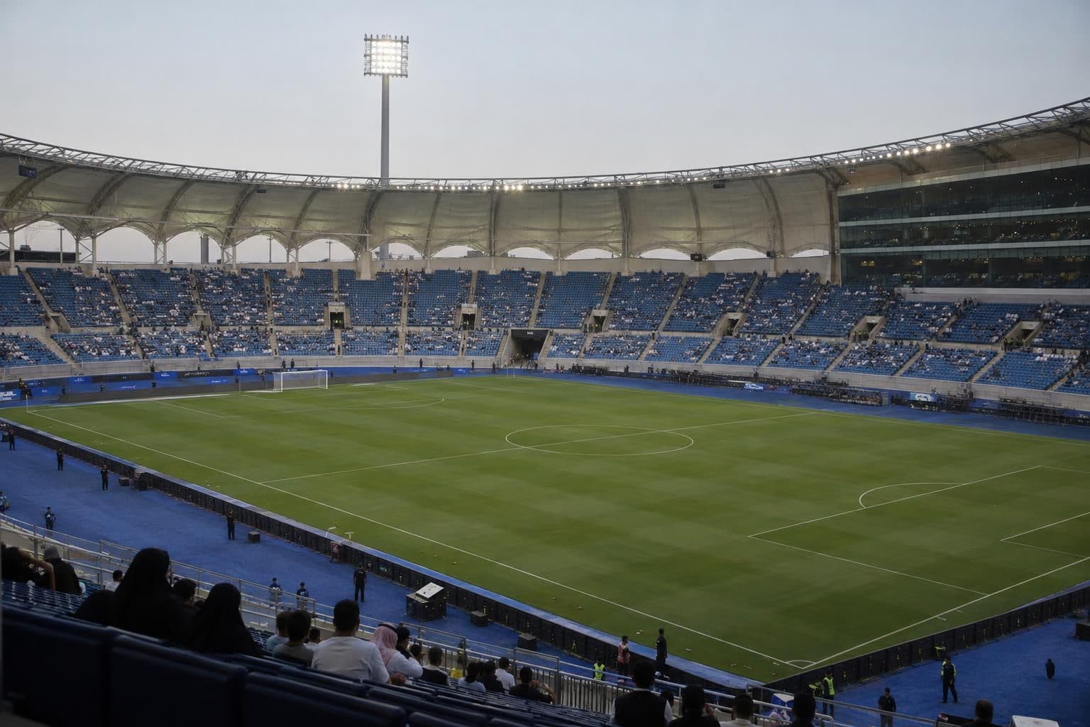 Sparse spectators remain seated in a football stadium during a match delay.