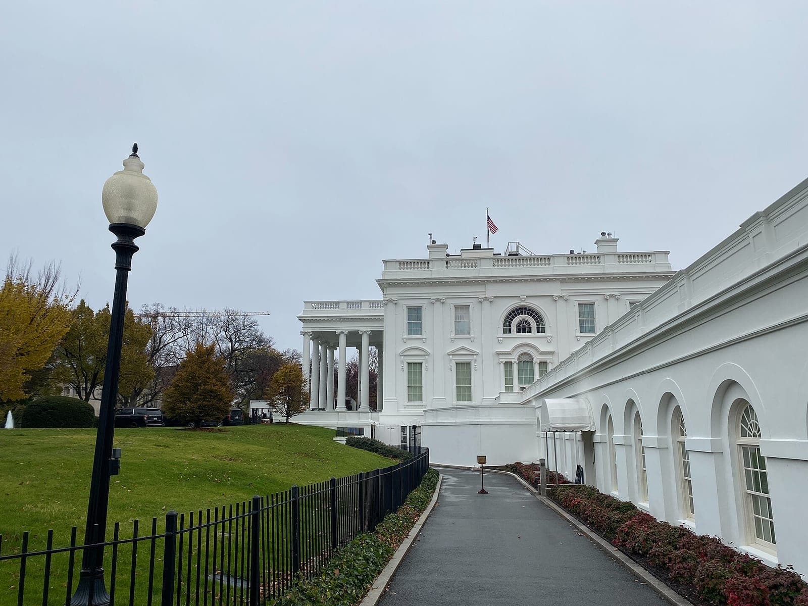 A white building with columns and arched windows stands beside a path, lawn and black fence.