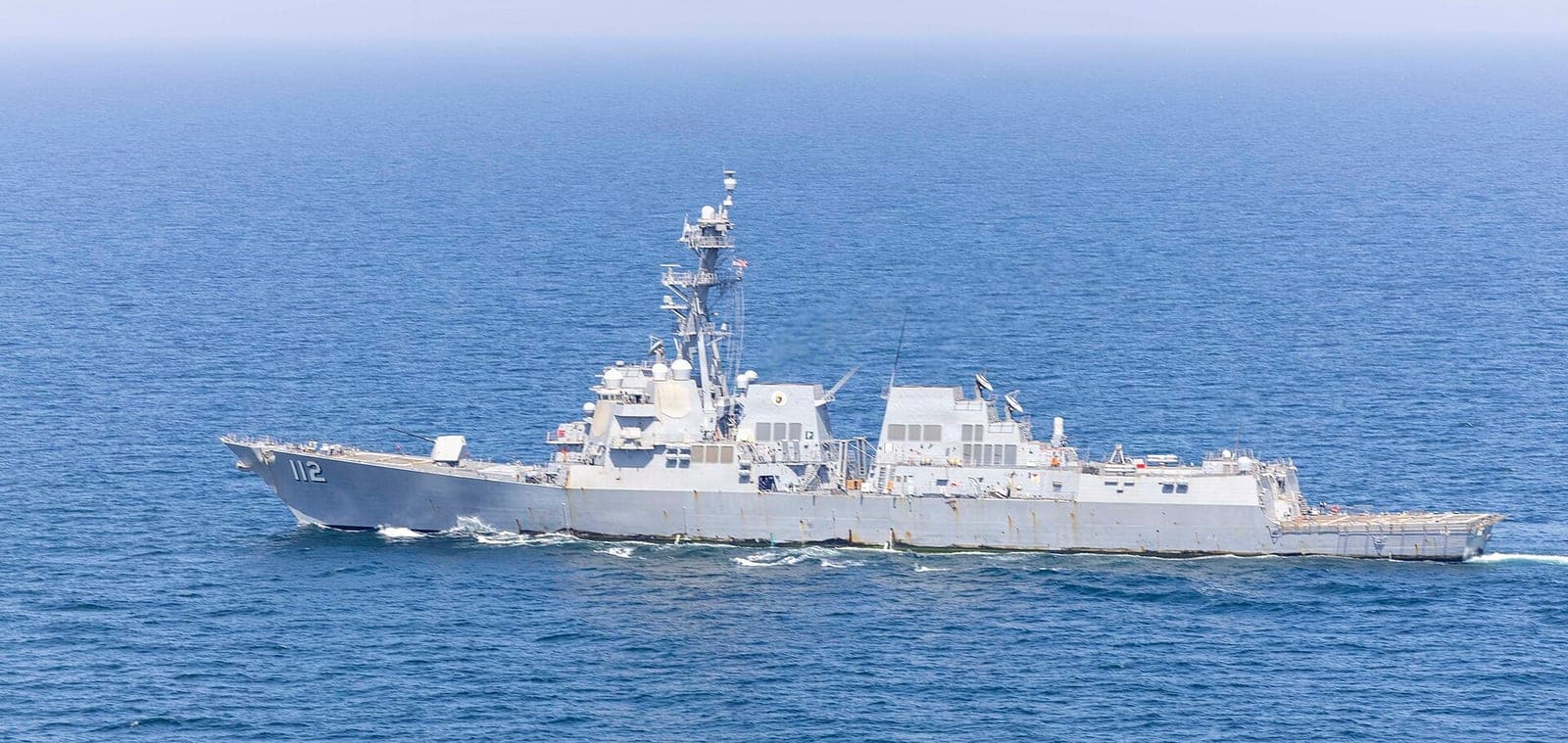 A gray naval destroyer marked 112 underway on blue open water.